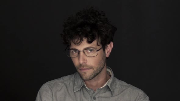 Man wearing glasses, slowly looking up at camera and smiling alt