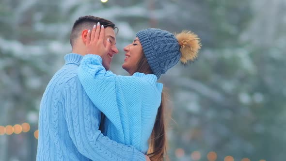Couple Hugs Standing on Outdoor Skating Rink with Garlands alt