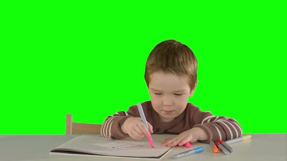 A Son Drawing at the Table at Home on a Green Screen alt