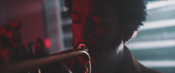 Close up of a trumpeter playing in backlit and red neon lights alt