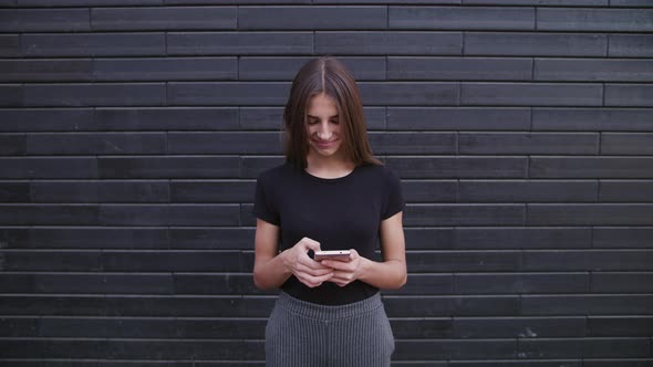 An Attractive Young Lady Wearing Glasses Using a Phone Against a Brick Wall Background. Close-up alt