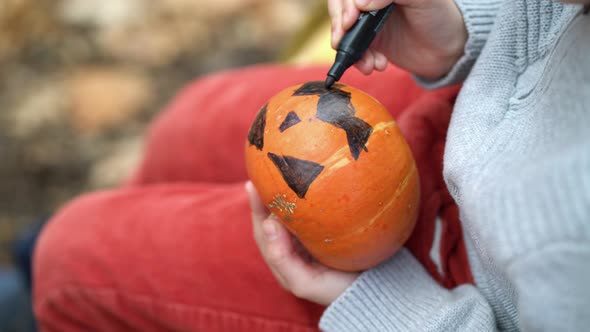 Close Up Boy Hands Paint Orange Pumpkin with Black Paint in Autumn Forest