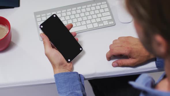 Caucasian businessman having video at desk using smartphone at desk in office alt