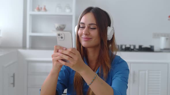 Close Up Woman in Darkblue Shirrt in Headphones Listening Music in Kitchen Background alt