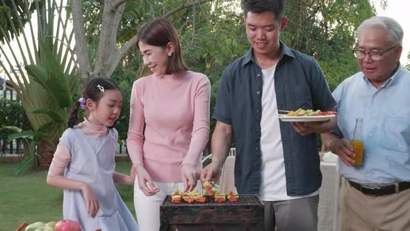 Happy Asian family having a barbecue-BBQ party together in the garden at home. alt