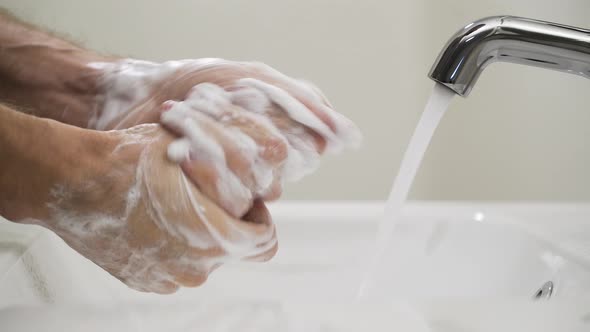 Person washing hands with soap in sink, avoid covid-19 coronavirus transmission alt