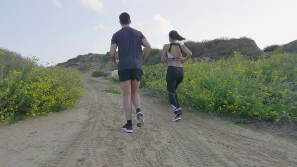 Track shot young sporty couple jogging together on country road alt