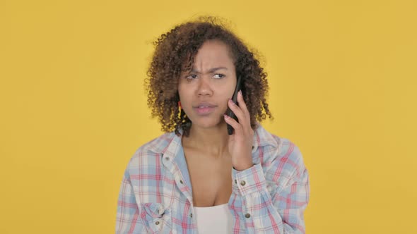 Young African Woman Talking Angry on Phone on Yellow Background alt