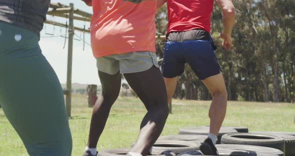 Diverse fit group running through tyres on obstacle course in the sun alt