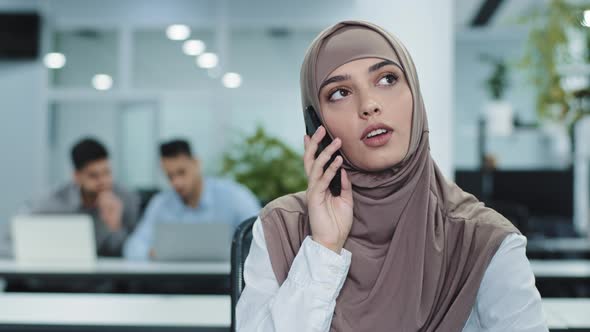 Serious Focused Arabic Female Millennial Manager in Hijab Talking on Phone Consulting Making alt