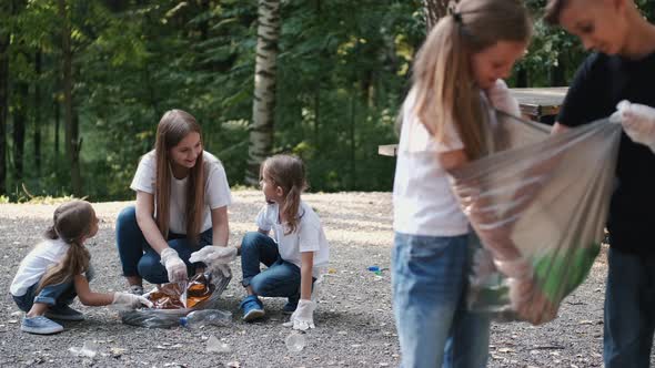 Group of Children with Young Volunteer Picking Up Rubbish in Forest alt