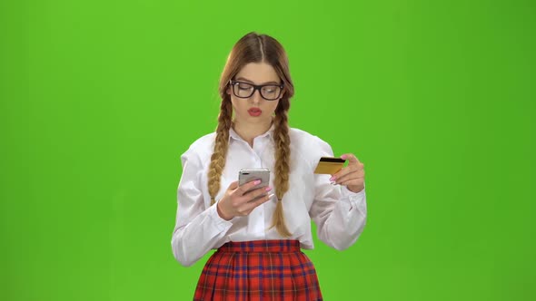 Girl in Glasses Dials Numbers on the Phone with a Gold Card. Green Screen alt
