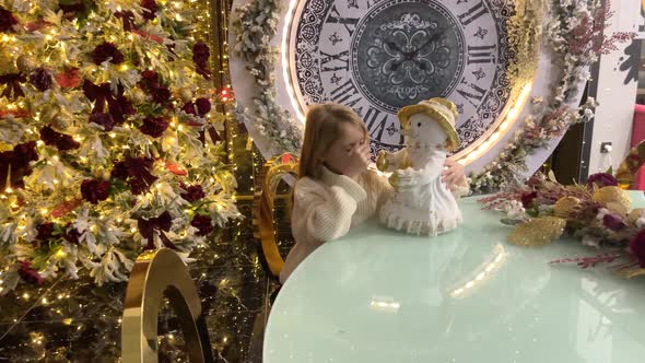 A Child Girl with a Snowman in Near a Christmas Tree with Big Clock alt