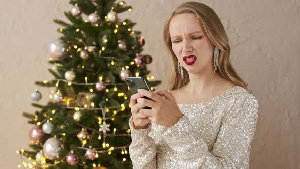 Angry festive blonde woman in a shiny evening dress typing on smart phone negative message alt