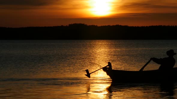 Beautiful Sunset Over Lake and Silhouette of Man Fishing from Boat
