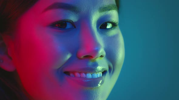 Young Millennial Japanese Woman Turning Face to Camera and Smiling Posing in Bright Colorful Neon alt