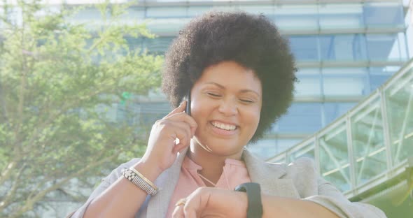 Happy plus size biracial woman checking smartwatch and walking in city alt