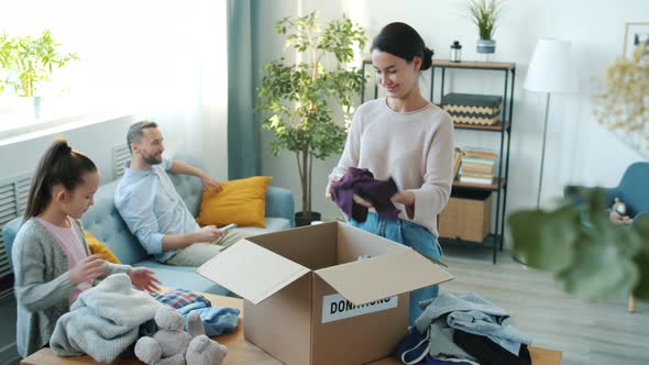 Selfless Mother and Daughter Collecting Clothing for Donation Packing Box Indoors in Apartment alt