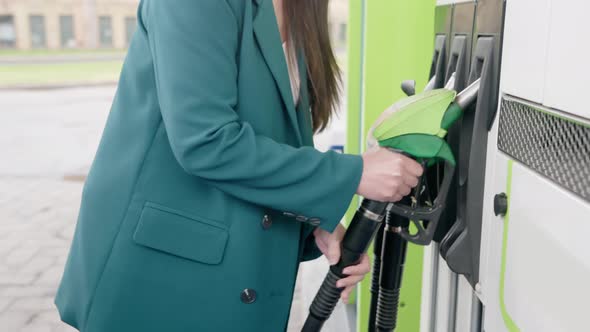 A business woman inserts a pistol into the tank to fill the car with gasoline or diesel