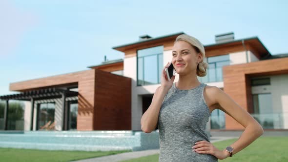 Successful Woman Talking Mobile Near Luxury House. Happy Woman Calling Phone alt