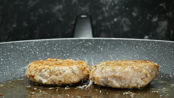 Dried Rosemary Falls on Roasting Meat Cutlets in a Frying Pan Closeup