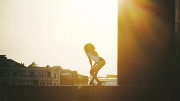 A Young Woman with Curly Hair Performing Attractive Strip Dancing on a Background of Buildings - alt