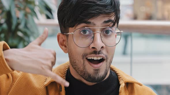 Closeup Young Smiling Flirting Indian Man Looking at Camera Holding Telephone with Hand Gesture Near alt