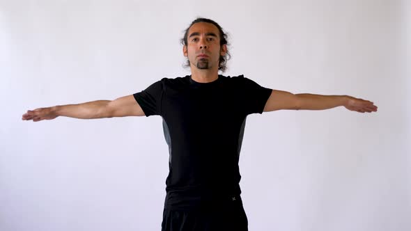 Hispanic Man with Long Hair and Goatee Doing Circular Shoulder Stretches Against White Studio Backdr alt