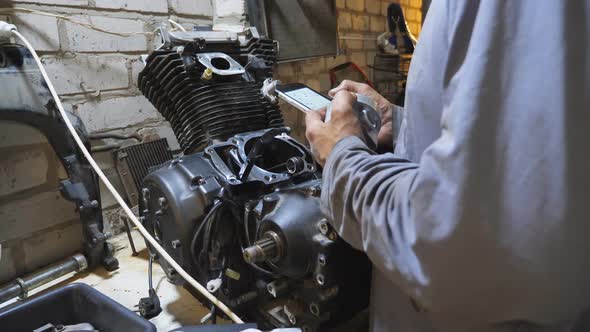 Male Hands of Mechanic Searching Properties and Characteristics of Vehicle Detail on Smartphone at alt