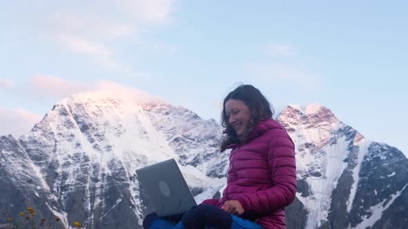 Young Happy Freelance Woman in the Mountains Calls Up Her Friends Via Video Link Via a Laptop and alt
