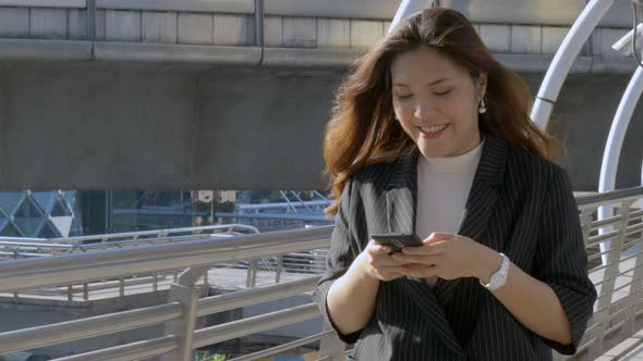 Asian woman walking texting with a friend on smartphone at urban city.