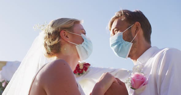 Portrait of happy caucasian newly wed couple touching heads at altar, wearing face masks alt