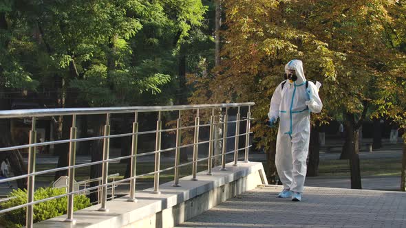 Man in a White Protective Suit Disinfects Handrails and Railings in a Public Area on a Deserted alt