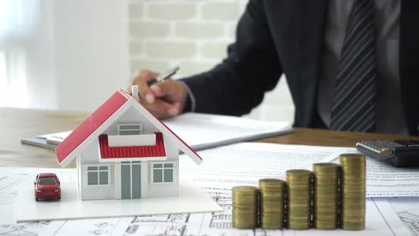 Businessman signing document after calculating expense with money and house model on the table