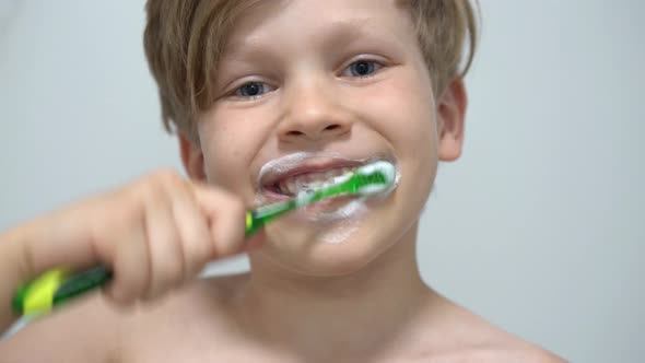 Cheerful Little Boy Brushing Teeth in Front of the Bathroom Mirror