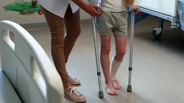 Female doctor assisting girl to walk with crutches alt