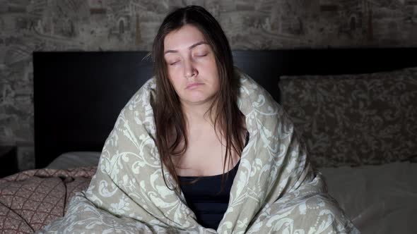 Brunette Woman Sits with a Sad Look on the Edge of the Bed and Yawns alt