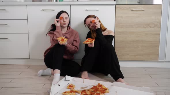 Happy Young Girls Eat Pizza and are Crooked Sitting at Home in the Kitchen