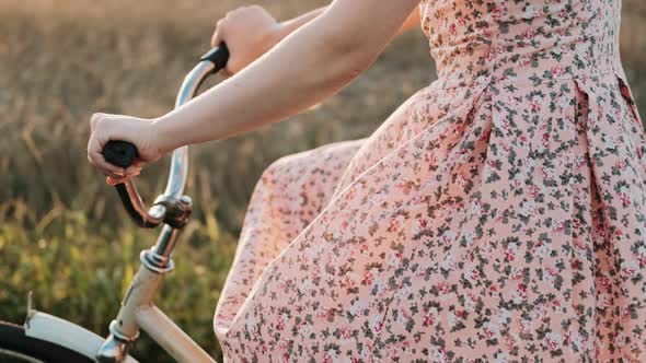 A Girl on a Bicycle is Riding a Field Road at Sunset alt