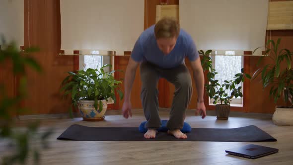 Handsome Young Man Approaching Yoga Mat Switching on Laptop to Be Ready Doing Yoga in Living Room at alt