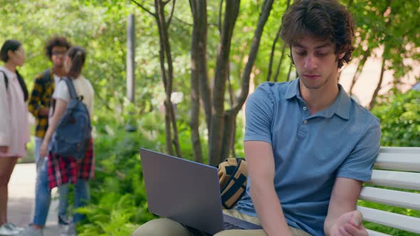 Young Man Sitting on Park Bench with Laptop Cleaning Hands with Sanitizer alt