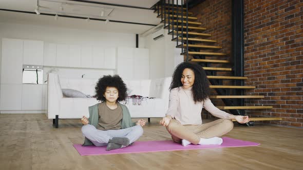 Mixed Rasa Preschool Boy Fools Around and Sits on the Carpet While His Young Mother Meditates in the alt