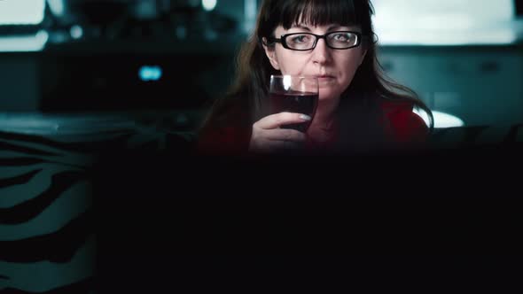 Cinematic Brunette Woman Relaxes with a Glass of Wine in Front of the TV in the Evening Woman After