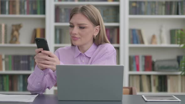 Woman Using Smartphone While Using Laptop in Office alt