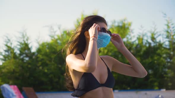 Young Fit Woman Wearing Black Bikini Top and Face Mask Fixing Her Sunglasses alt