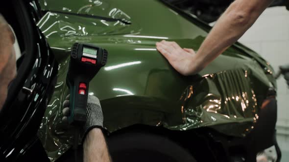 Two Men are Vinyl Wrapping a Car in Dark Green Color Using Heat Gun