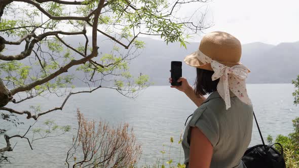 Tourist with beautiful straw hat taking pictures of the famous lake maggiore. alt