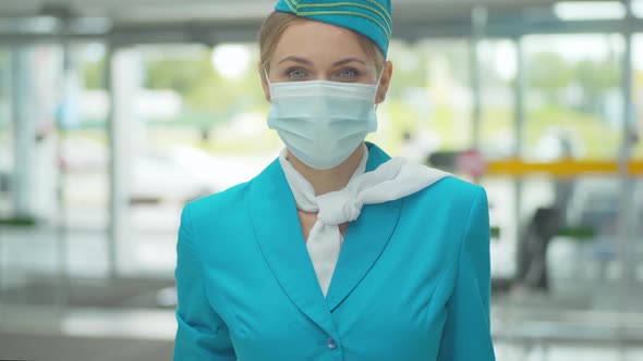 Young Stewardess in Uniform and Face Mask Looking at Camera and Smiling. Portrait of Positive alt