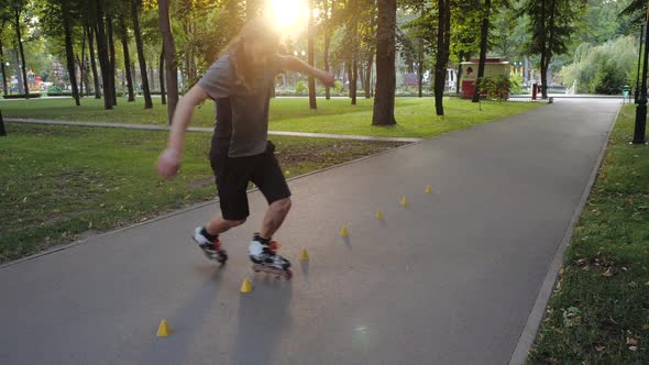 Young Long-haired Bearded Man Roller Skater Is Dancing Between Cones in a Nice Evening in a City alt