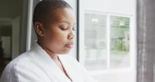 Thoughtful african american plus size woman wearing robe, looking through window alt
